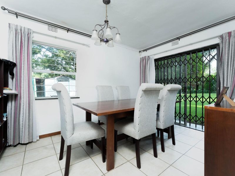 A functional dining room featuring tiled flooring, a sliding glass door with security gate, and direct access to the garden area.