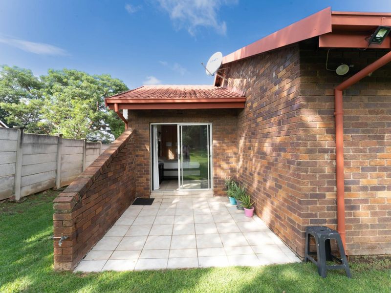 A rear exterior view featuring a paved patio area, brick wall construction, and a sliding glass door entrance to the home.