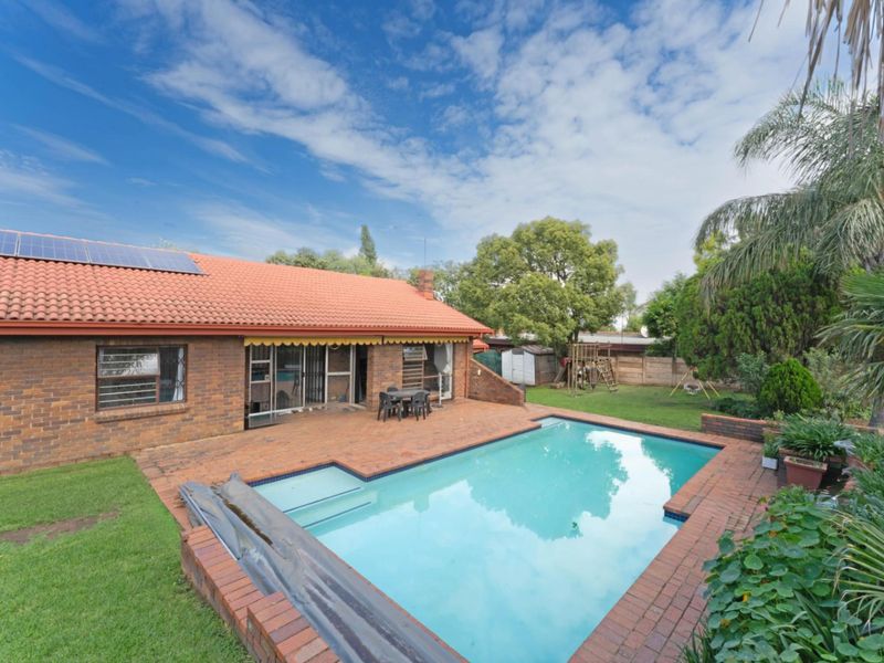 Rear view of the property featuring a brick patio, swimming pool, and a tiled roof with installed solar panels.