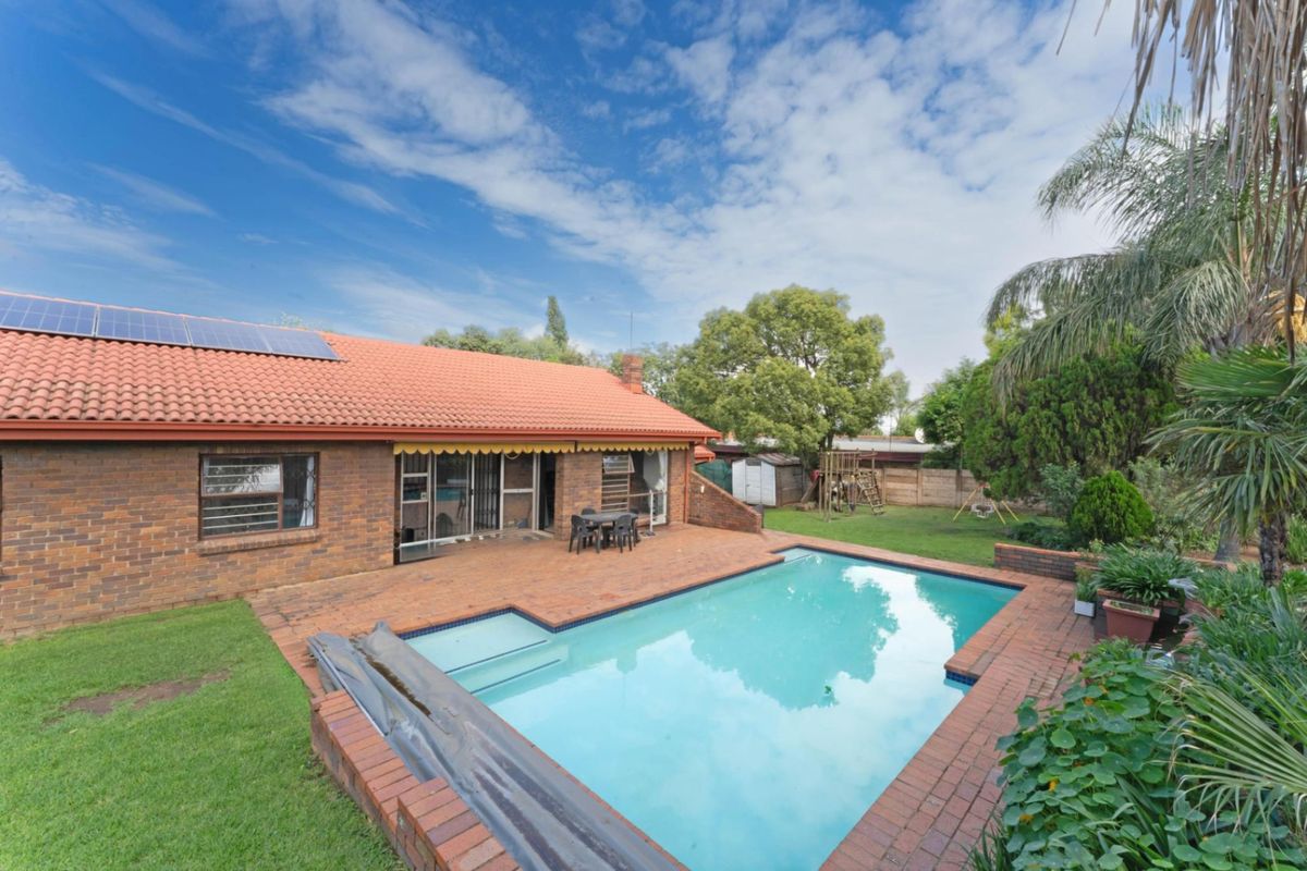 Rear view of the property featuring a brick patio, swimming pool, and a tiled roof with installed solar panels.