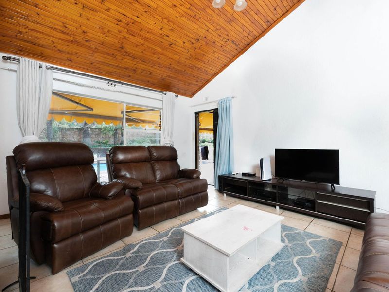 Spacious living room featuring a high vaulted timber ceiling, tiled flooring, and direct access to the outdoor patio area through sliding glass doors.