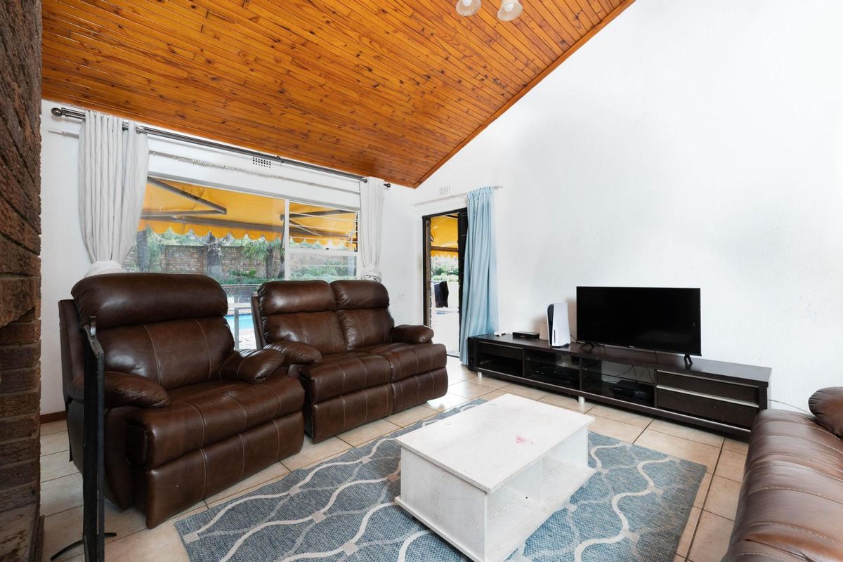 Spacious living room featuring a high vaulted timber ceiling, tiled flooring, and direct access to the outdoor patio area through sliding glass doors.