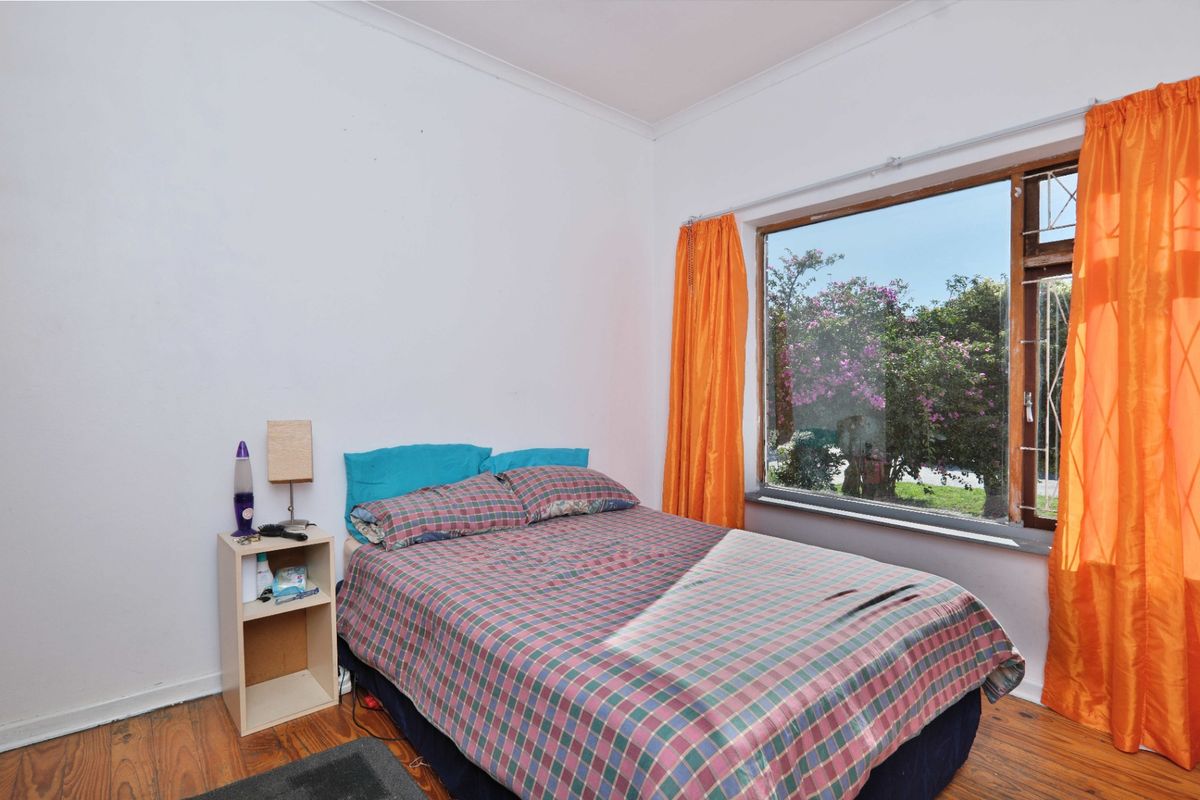 A bedroom featuring timber flooring and a large window with security bars, offering natural light and garden views.