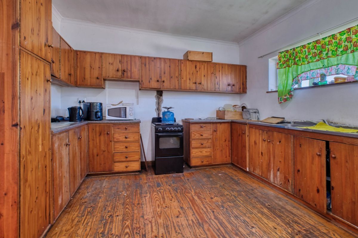 A dated kitchen featuring original timber cabinetry, worn wooden flooring, and a freestanding oven, offering significant potential for a modern renovation.