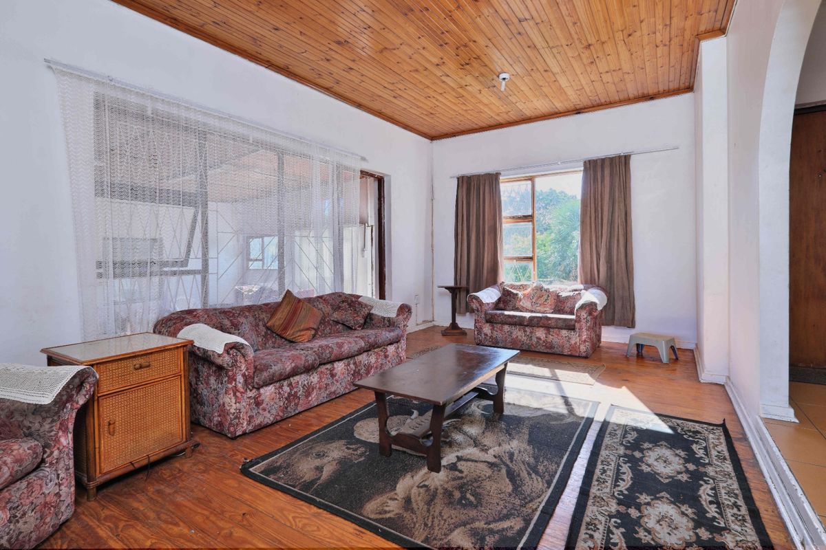 Spacious living room featuring timber ceilings, wooden flooring, and large windows providing natural light and access to an adjoining sunroom area.