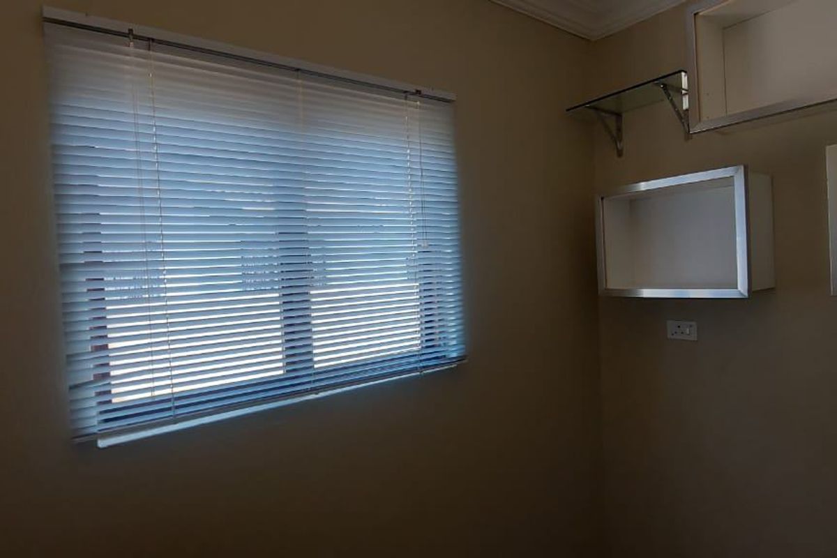 A neutral-toned bedroom featuring built-in wall shelving and venetian blinds, offering a clean and versatile space ready for personalization.