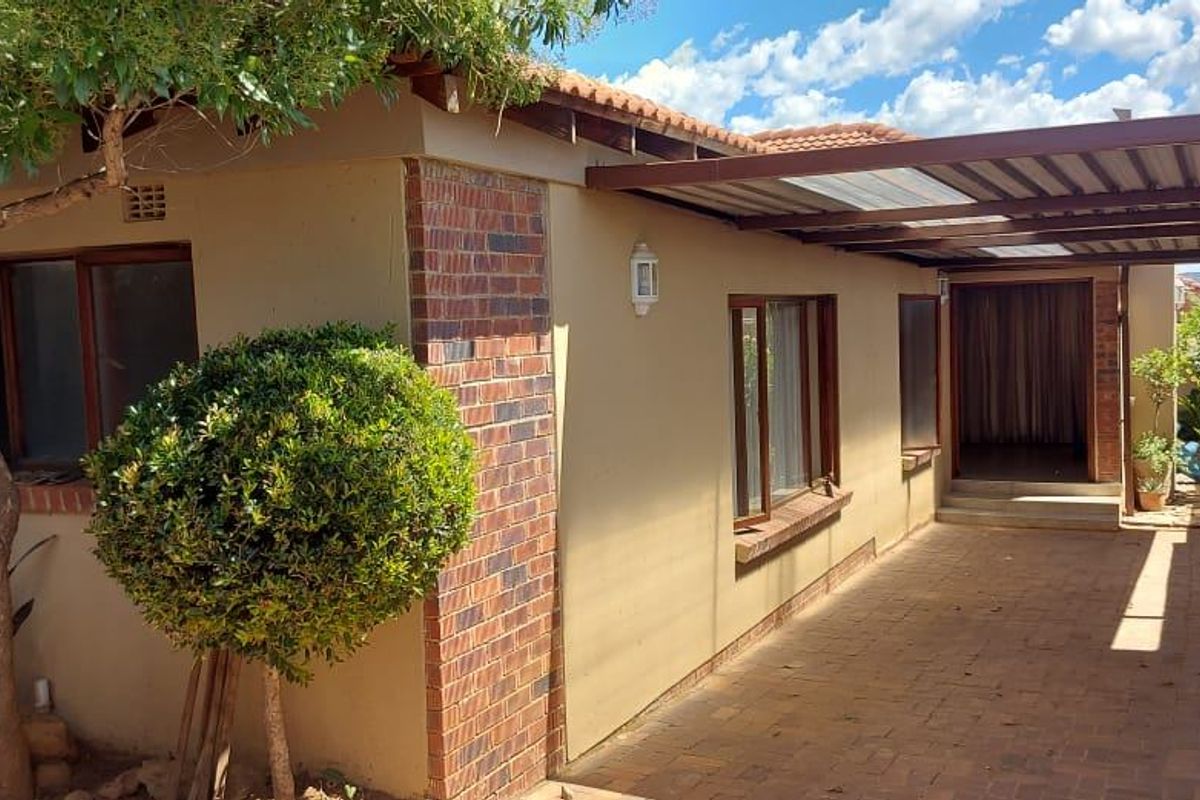A rear exterior view of the house featuring a paved driveway, covered patio area, and established garden elements.