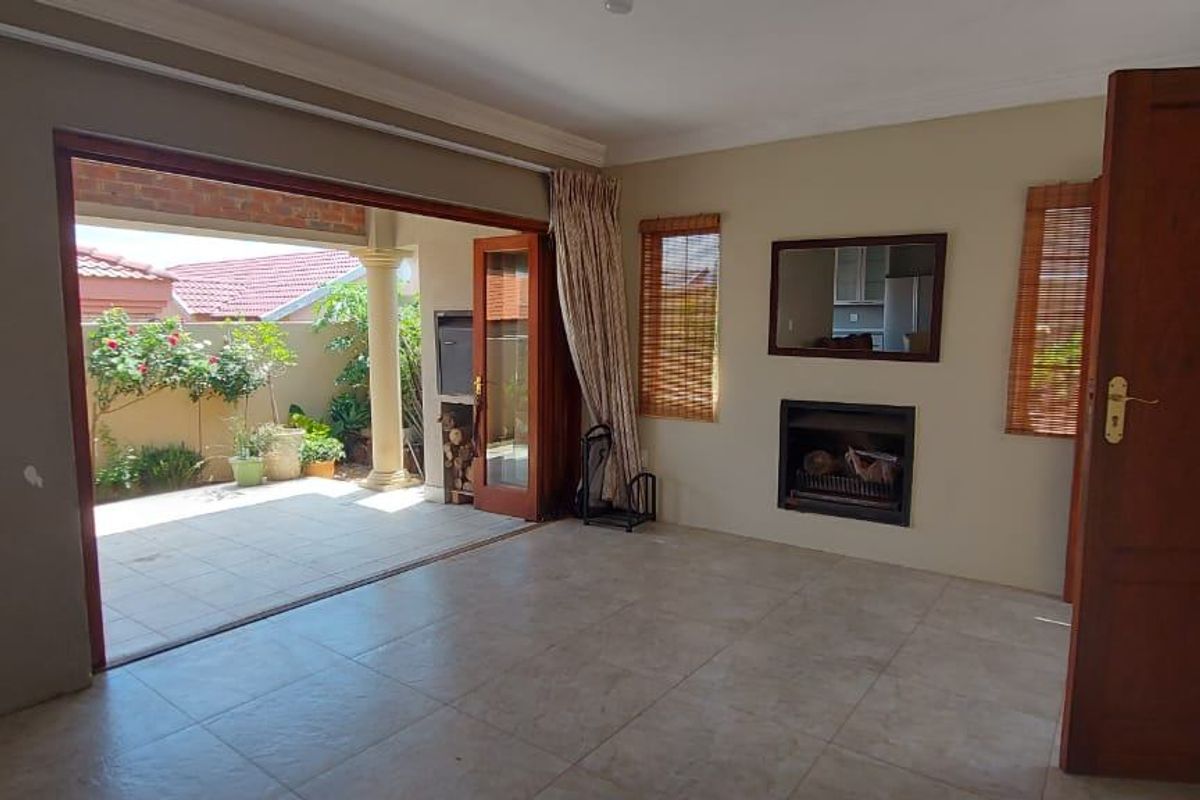 Spacious living room featuring tiled floors, a built-in fireplace, and large sliding doors opening onto a covered patio with a built-in braai.