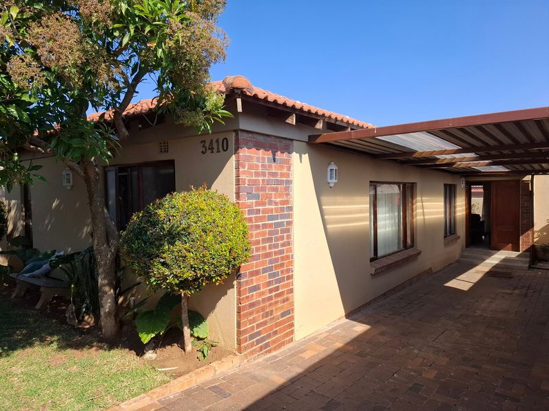 Front exterior view of the house featuring a paved driveway, covered carport, and a combination of brick and rendered wall finishes.