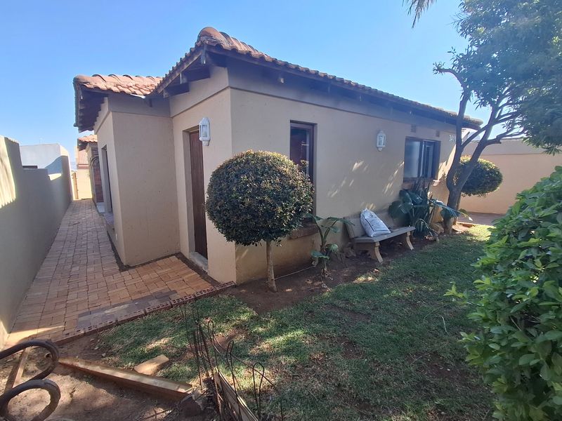 Rear exterior view of the house featuring a paved walkway, terracotta roof tiles, and established garden area.