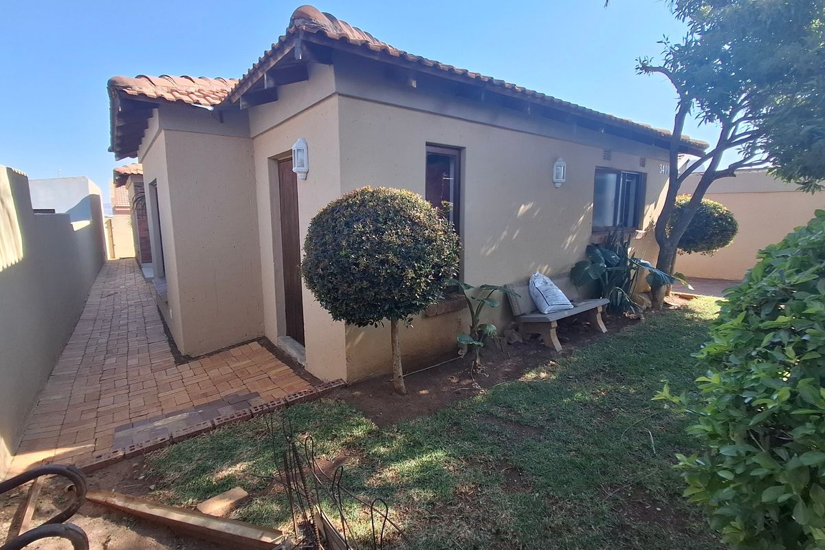 Rear exterior view of the house featuring a paved walkway, terracotta roof tiles, and established garden area.