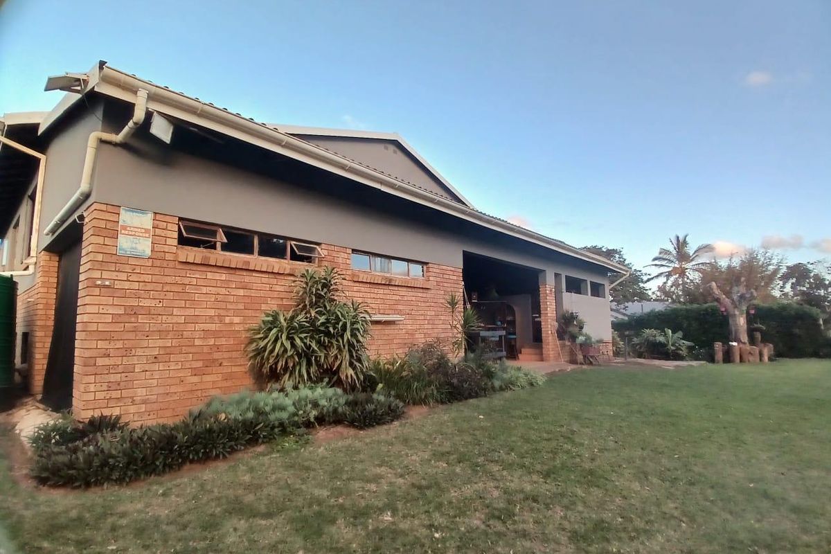 Rear view of the house featuring a brick and plaster facade, tiled roof, and a covered patio area overlooking the garden.
