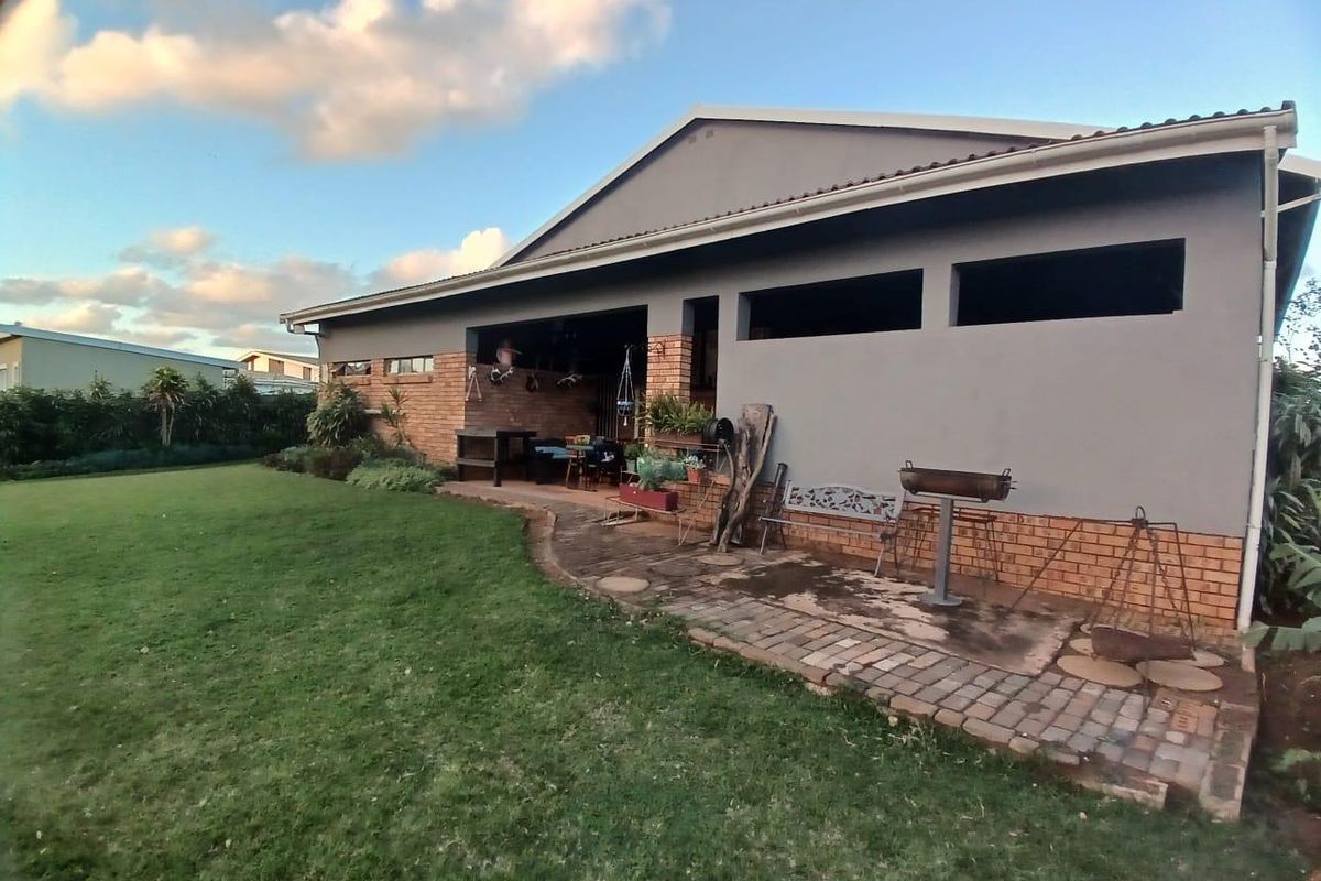 Rear view of the property featuring a covered patio area, brick exterior walls, paved walkway, and a spacious lawn.
