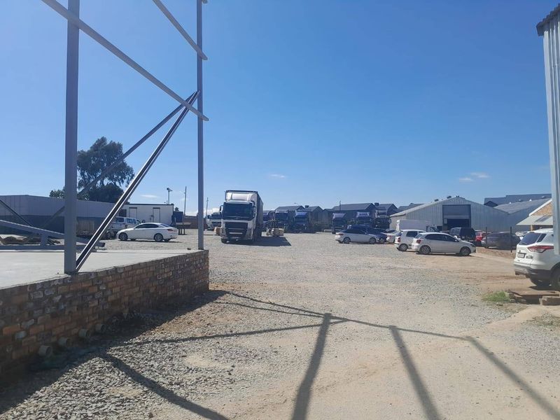 A spacious commercial yard featuring a gravel surface, brick foundation plinth, and exposed steel structural framing for a warehouse or industrial building.