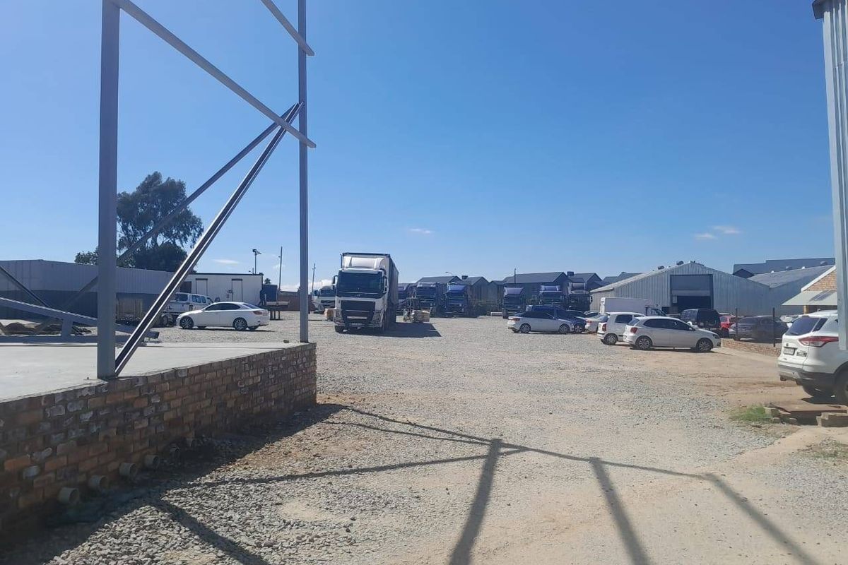 A spacious commercial yard featuring a gravel surface, brick foundation plinth, and exposed steel structural framing for a warehouse or industrial building.