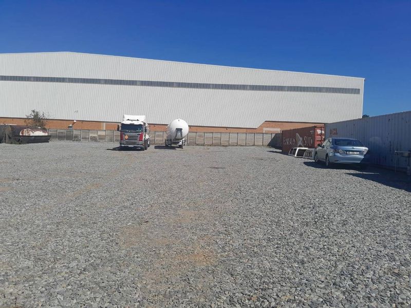 A large industrial warehouse facility featuring a spacious gravel yard area suitable for logistics or storage operations.