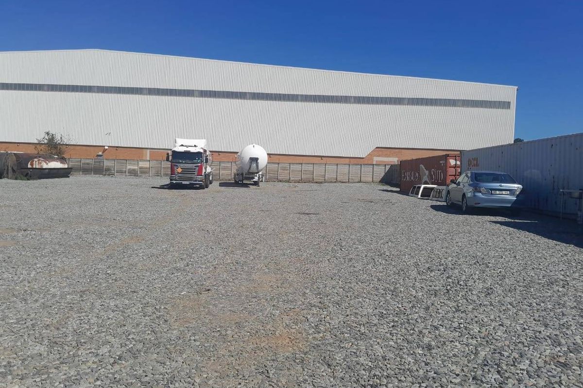 A large industrial warehouse facility featuring a spacious gravel yard area suitable for logistics or storage operations.