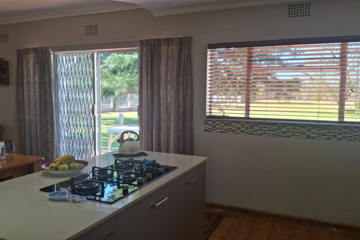 A functional kitchen featuring a central island with a built-in gas hob, mosaic tile splashback, and direct access to the garden through sliding doors.