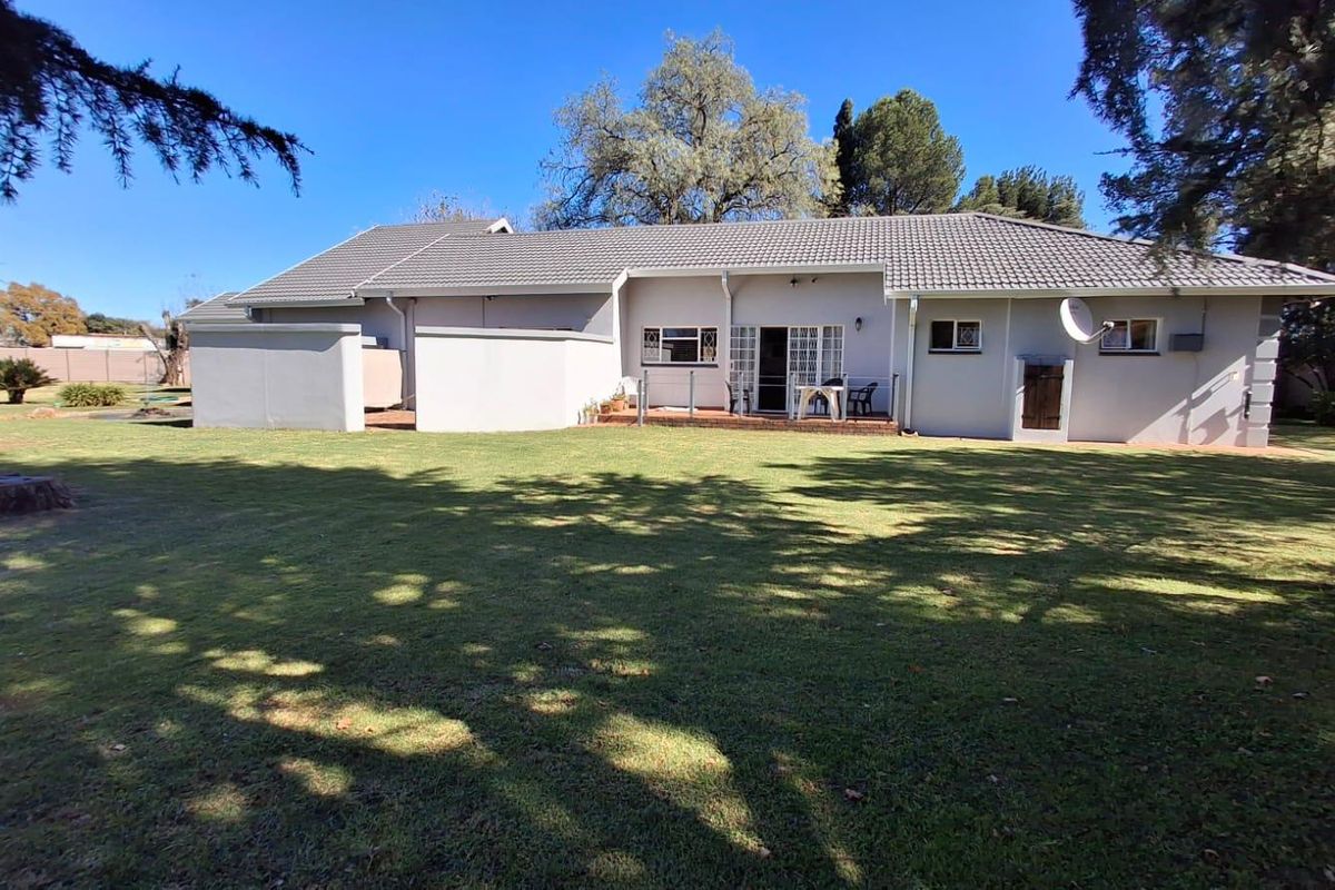 Rear view of the house featuring a tiled roof, a paved patio area, and a spacious, well-maintained lawn.