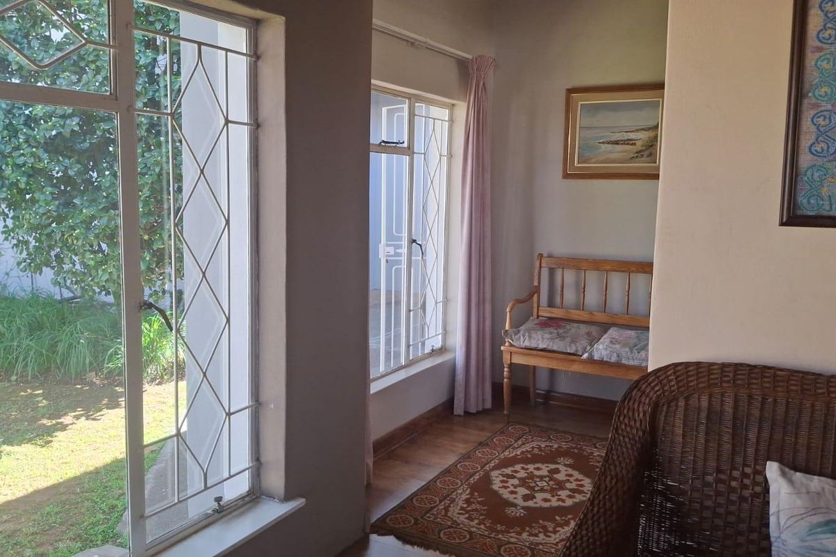 A sunlit living area featuring timber flooring and large windows with security bars, offering a pleasant view of the garden.