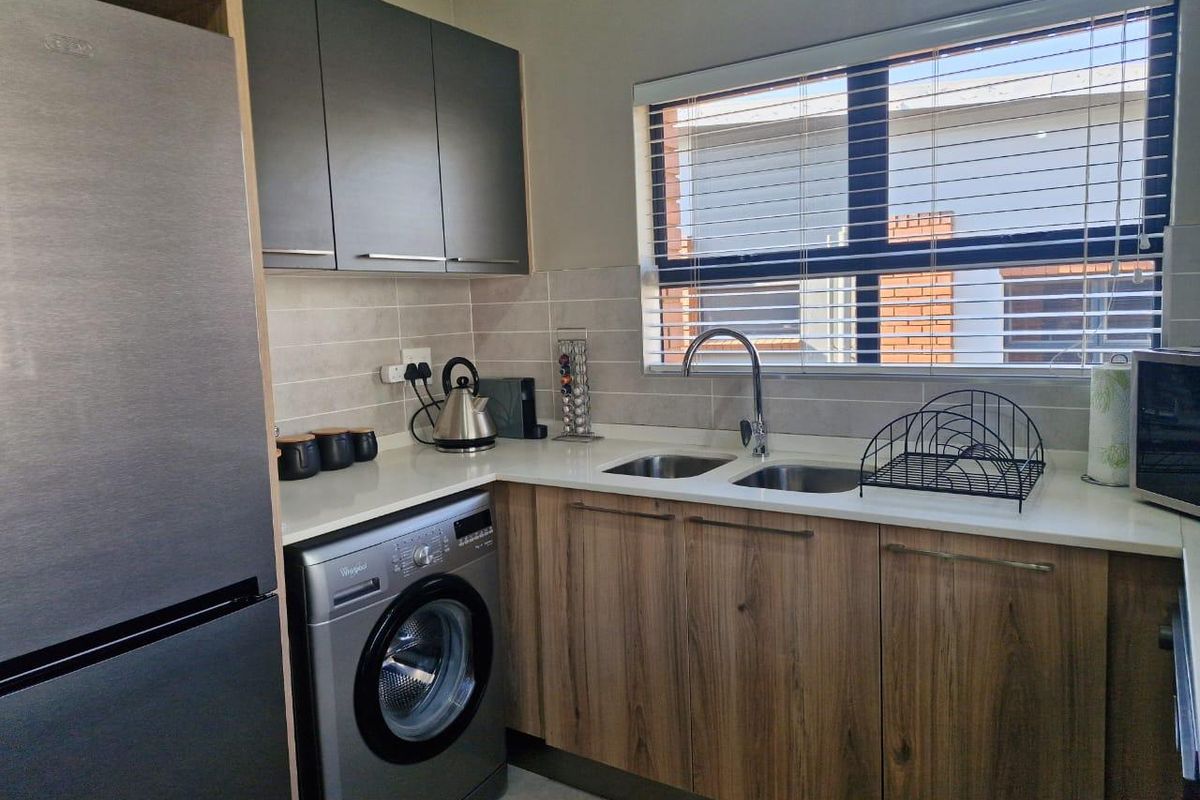 A modern, well-maintained kitchen featuring wood-finish lower cabinetry, sleek grey upper cabinets, stone countertops, and a double basin sink with a window view.