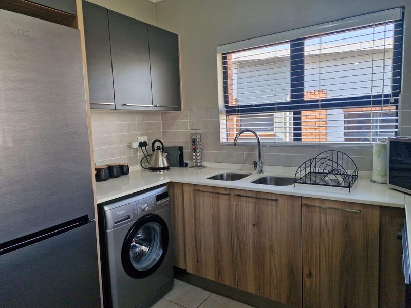 A modern, well-maintained kitchen featuring wood-finish lower cabinetry, sleek grey upper cabinets, stone countertops, and a double basin sink with a window view.