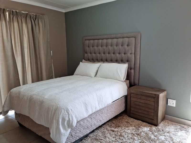 A well-maintained bedroom featuring neutral wall tones, tiled flooring, and a modern tufted headboard.