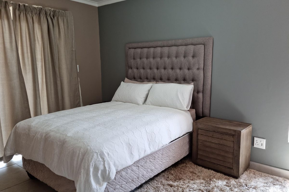 A well-maintained bedroom featuring neutral wall tones, tiled flooring, and a modern tufted headboard.
