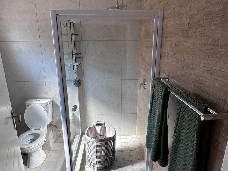 A modern bathroom featuring a glass-enclosed shower, a standard toilet, and contemporary tiled wall finishes with a wood-look accent wall.
