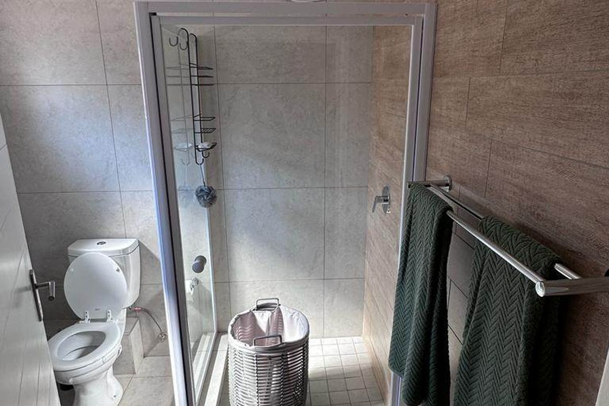 A modern bathroom featuring a glass-enclosed shower, a standard toilet, and contemporary tiled wall finishes with a wood-look accent wall.