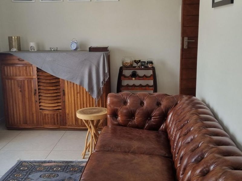 A well-maintained living room featuring neutral tiled flooring, a large window allowing natural light, and a solid wooden door.