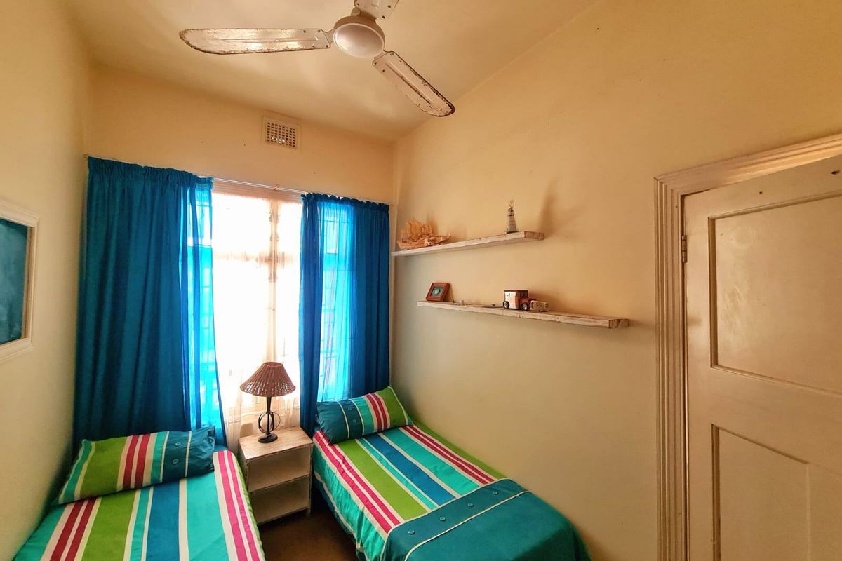 A compact bedroom featuring a ceiling fan, built-in wall shelving, and a traditional timber door, offering a functional space with potential for cosmetic updates.