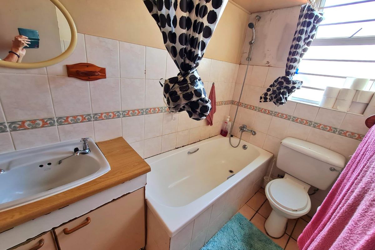 A functional bathroom featuring a built-in vanity, bathtub with shower mixer, and toilet, finished with tiled walls and flooring.