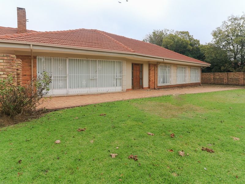 Rear view of a single-story brick house featuring a tiled roof, paved patio area, and a large garden with brick boundary walling.