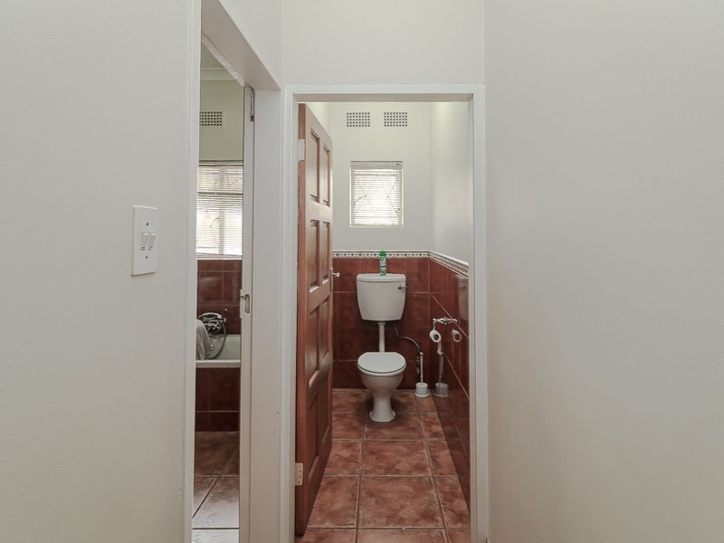 A functional bathroom featuring ceramic wall and floor tiles, a standard toilet, and a timber door, presenting a dated but well-maintained space.
