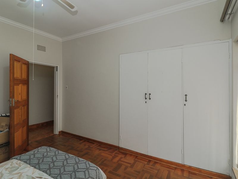 A bedroom featuring parquet flooring, built-in cupboards, a ceiling fan, and an air conditioning unit.