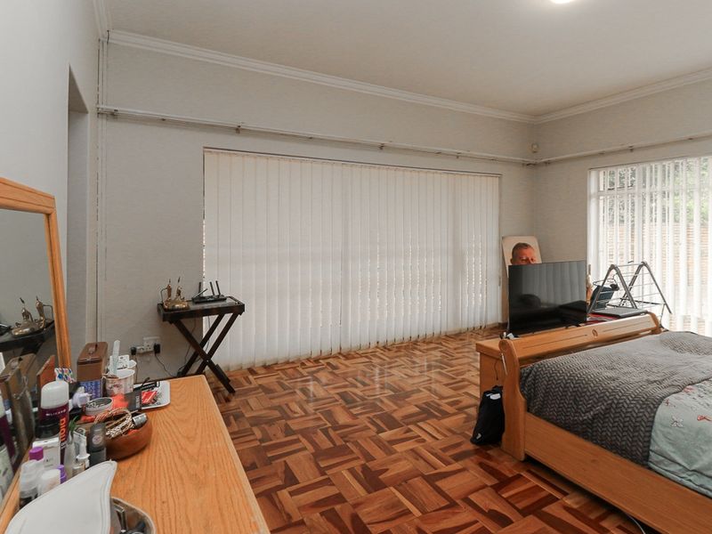 A spacious bedroom featuring classic parquet flooring, large windows with vertical blinds, and decorative cove cornicing.