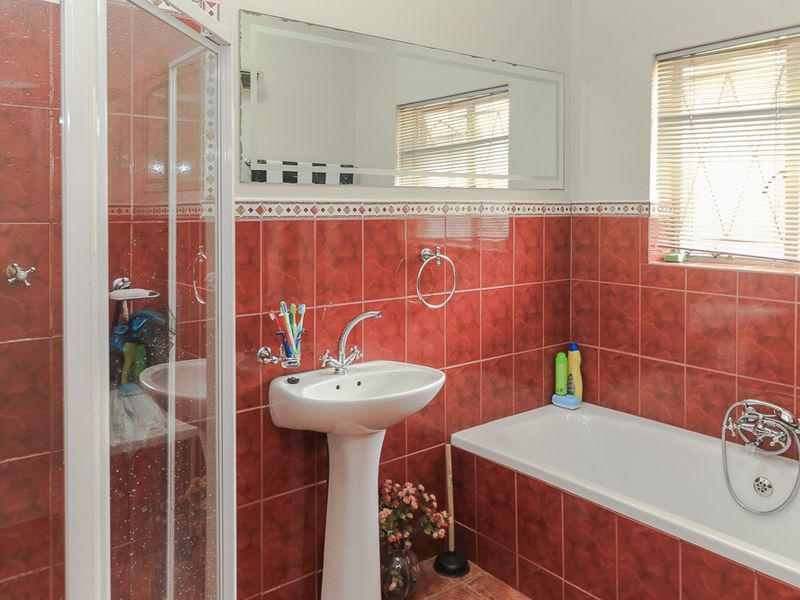 A functional bathroom featuring a pedestal basin, a separate shower enclosure, and a bathtub, finished with bold red wall tiling.