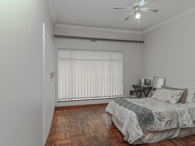 A well-maintained bedroom featuring classic parquet flooring, built-in storage cupboards, and a ceiling fan, providing a neutral and functional living space.