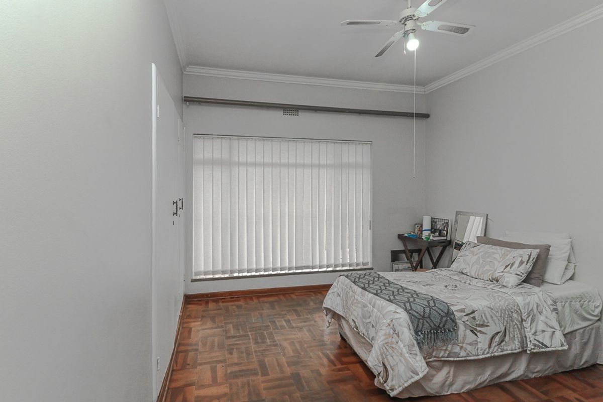 A well-maintained bedroom featuring classic parquet flooring, built-in storage cupboards, and a ceiling fan, providing a neutral and functional living space.