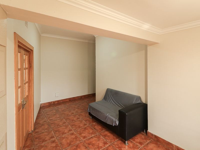 A neutral living area featuring ceramic floor tiles, coved ceiling cornices, and a timber door, offering a clean and functional space.