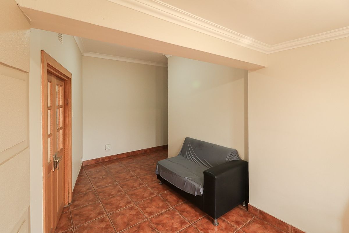 A neutral living area featuring ceramic floor tiles, coved ceiling cornices, and a timber door, offering a clean and functional space.
