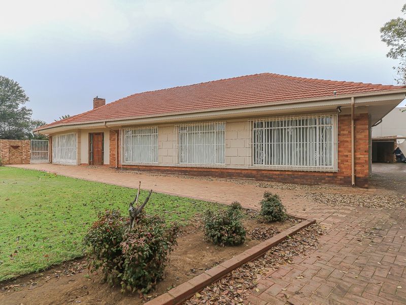 Rear view of a single-story brick house featuring a terracotta tiled roof, security bars on windows, and a paved walkway leading to a lawn area.