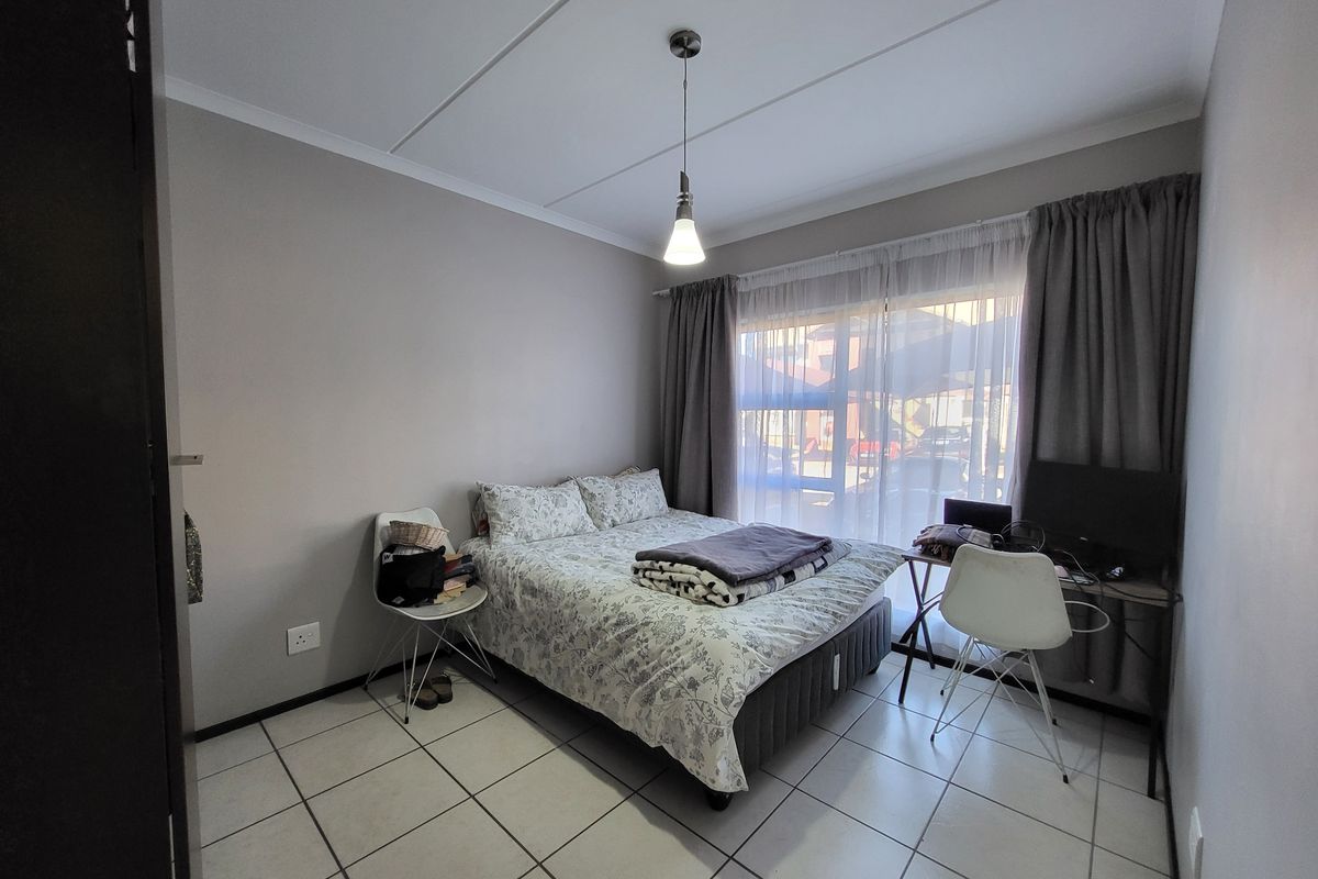 A functional bedroom featuring tiled flooring, a central pendant light, and large windows with curtain tracks, providing a neutral base for personalization.