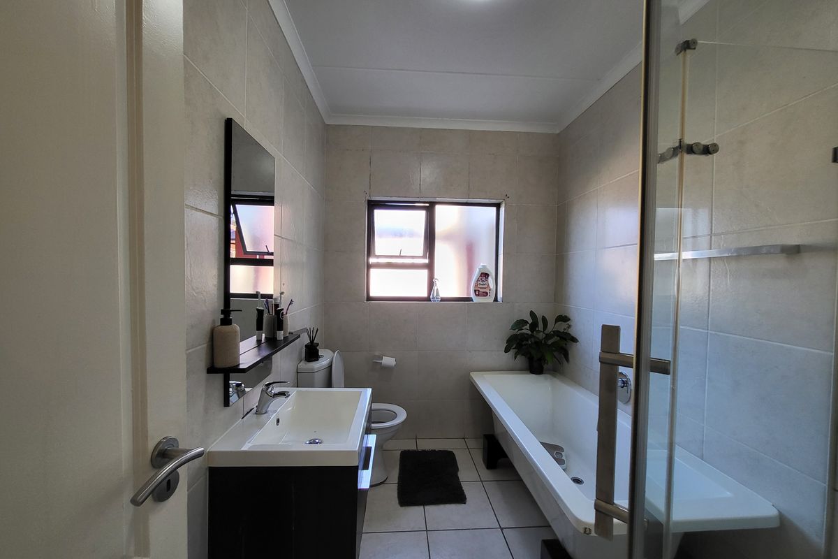 A well-maintained bathroom featuring a vanity with basin, a bathtub, a toilet, and a glass shower screen with neutral wall and floor tiling.
