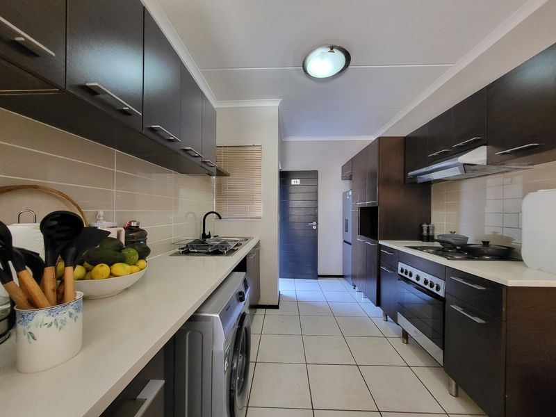Modern galley-style kitchen featuring dark wood cabinetry, stone countertops, built-in oven, gas hob, and tiled flooring with a clean, functional layout.