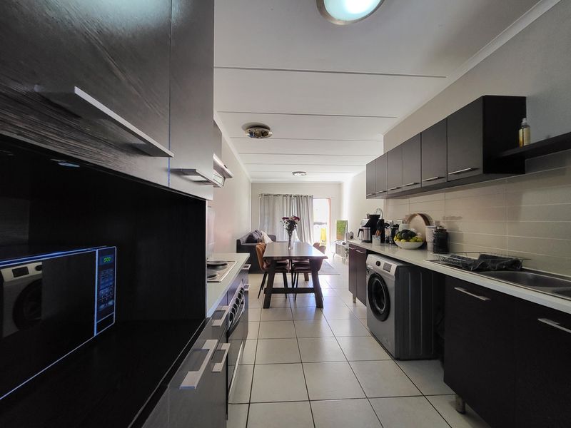Open-plan kitchen and living area featuring dark cabinetry, tiled flooring, and integrated appliances, leading to a dining space with natural light.