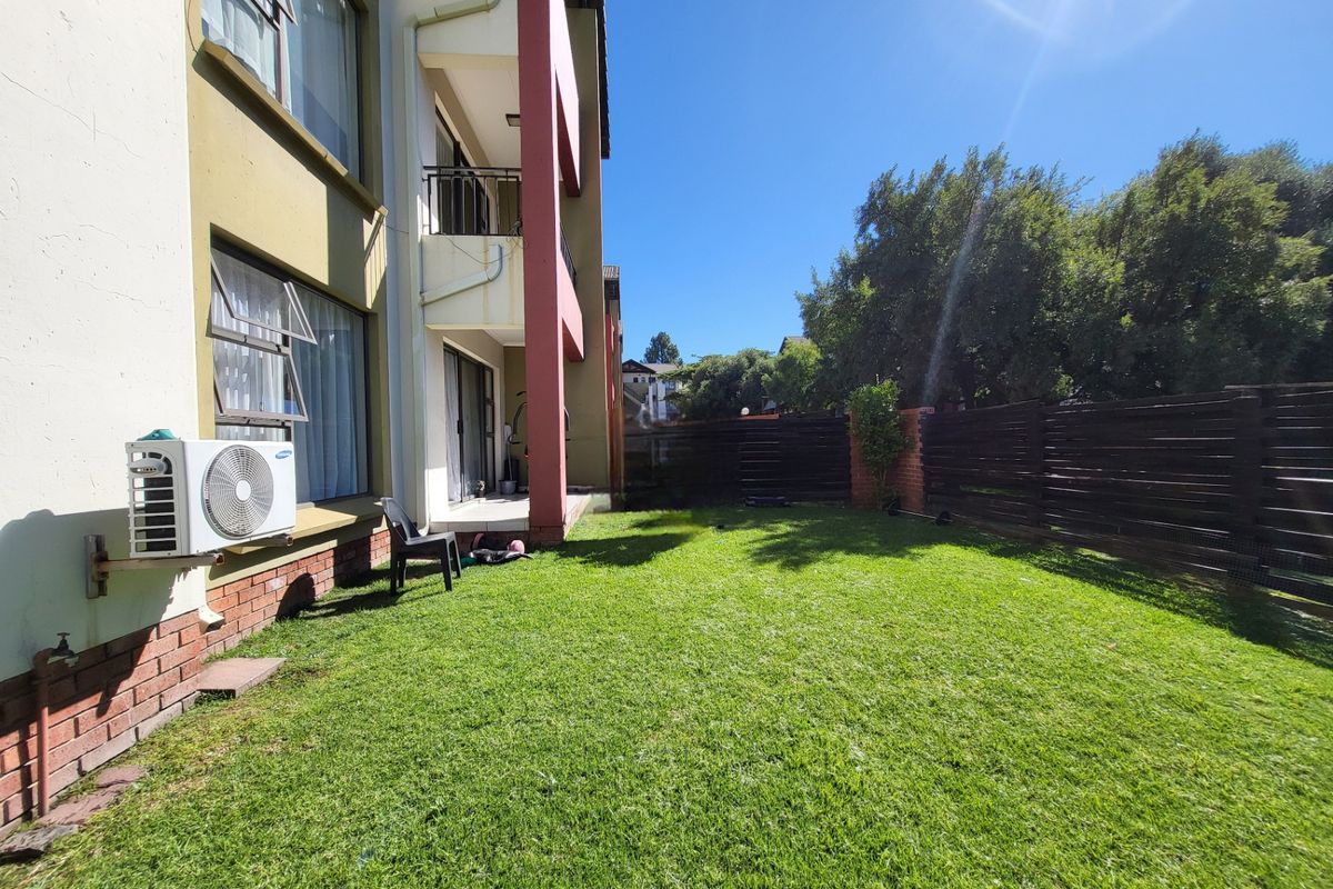 Rear view of the apartment building featuring a private garden, lawn area, timber boundary fencing, and an external air conditioning unit.