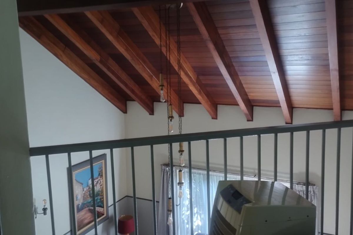 A mezzanine view overlooking the living area, featuring high vaulted timber ceilings with exposed rafters and a modern metal balustrade.