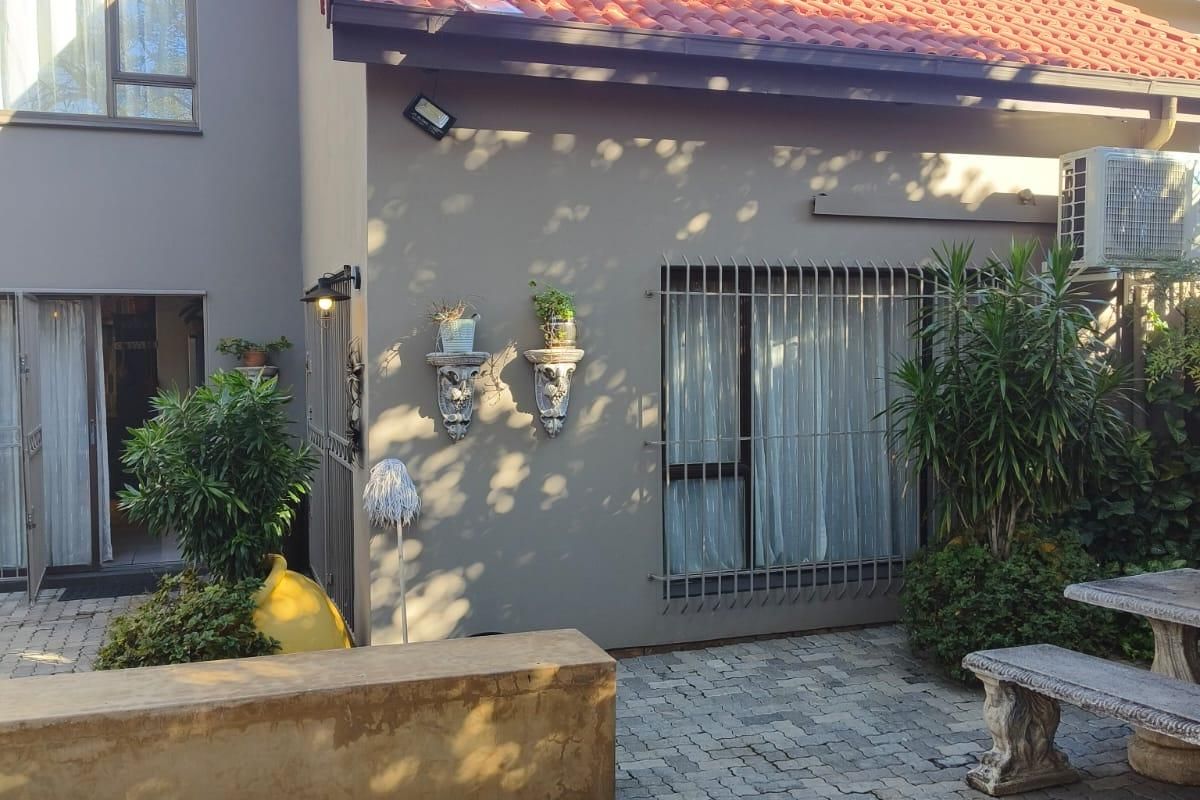 A rear exterior view of a townhouse featuring a paved patio area, security bars on windows, and a built-in concrete bench.